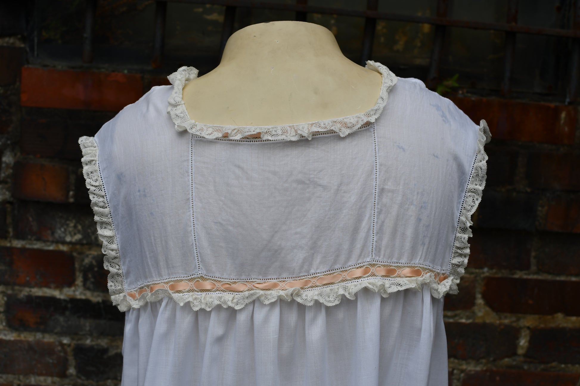 white lacy dress with lace details on a mannequin against a brick wall.